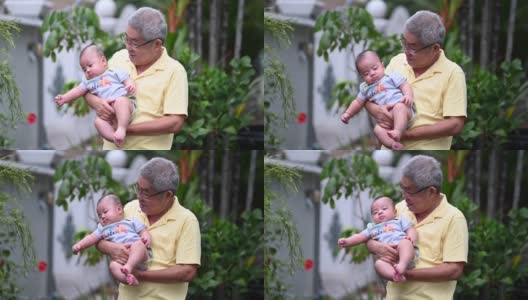 一位亚洲华人老人抱着他的小孙子站在他们家的前院高清在线视频素材下载