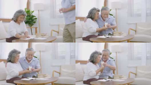 在老人院的客厅早上，亚洲爷爷和奶奶手拿杯子喝牛奶坐在那里开心地笑着聊天高清在线视频素材下载