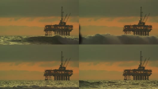 在一个戏剧性的，暴风雨的天空下的日落下，海浪撞击在地平线上的近海石油钻井平台在南加州亨廷顿海滩海岸高清在线视频素材下载