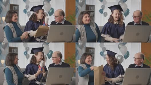 毕业证书在线，愉快的毕业生戴着帽子和长袍与父母一起庆祝大学毕业典礼期间通过视频连接坐在家里的笔记本电脑背景气球高清在线视频素材下载