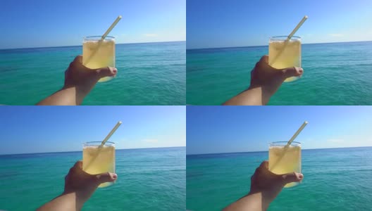 手握黄色明亮的夏季热带鸡尾酒与美丽的热带海洋高清在线视频素材下载