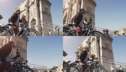 在阳光明媚的一天，三个年轻的朋友骑着自行车在罗马市中心的罗马圆形大剧场康斯坦丁拱门附近散步高清在线视频素材下载