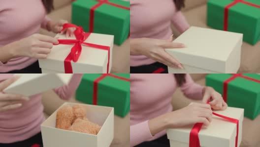 女人靠近手打开礼物盒子，把泰迪熊放在盒子里。年轻快乐可爱的女孩庆祝在圣诞节节日与许多礼品盒坐在家里的沙发上高清在线视频素材下载
