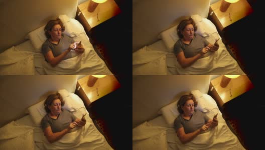 老妇人睡前躺在床上使用智能手机高清在线视频素材下载