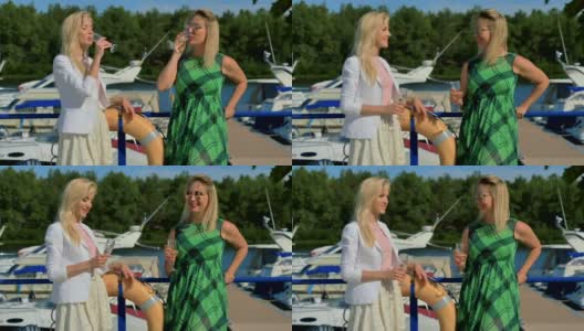 两个时髦的女人聊天和喝香槟站在游艇俱乐部的背景高清在线视频素材下载