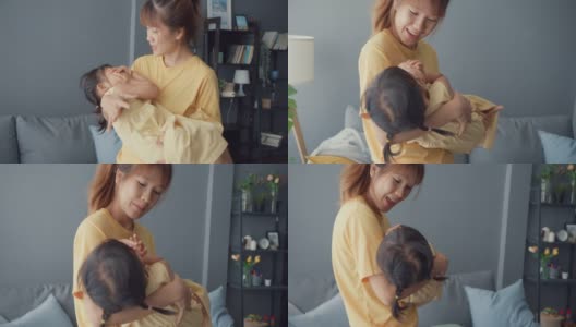 快乐开朗的亚洲家庭妈妈抱着蹒跚学步的小女孩在怀里哭泣，在家里的客厅里安慰呵护着。高清在线视频素材下载