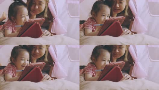 一张专注于亚洲妈妈和可爱的女儿躺在家里粉色帐篷的地板上，在使用数字技术的平板电脑上写着快乐和快乐的时刻。高清在线视频素材下载