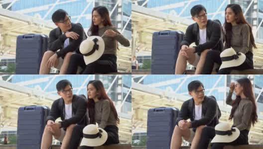 年轻的亚洲夫妇旅行者和行李坐在城市交谈。情人旅游者在假期外出旅游。高清在线视频素材下载