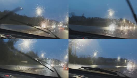 特写大雨落在汽车的挡风玻璃上，雨刷工作迅速。雨点从汽车前窗倾泻而下。开着前灯的汽车在高速公路上开会。4 k的片段高清在线视频素材下载