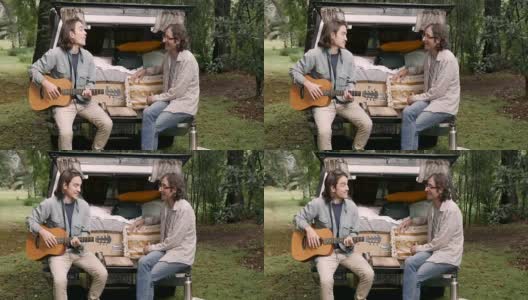 两个留着长发拿着吉他的男人坐在一辆卡车的后挡板上聊天高清在线视频素材下载