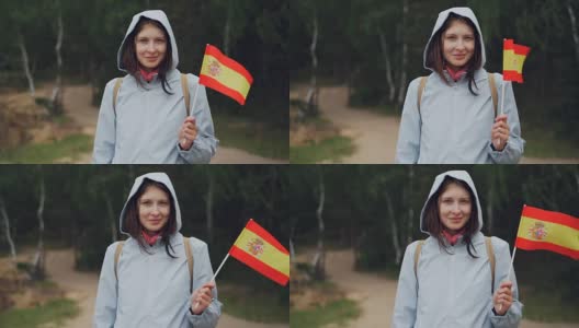 慢动作肖像的快乐世界旅行者漂亮的女孩在帽外套挥舞西班牙国旗和看着镜头微笑。国家和旅游概念。高清在线视频素材下载