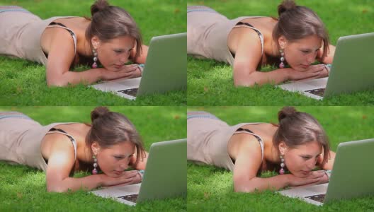 微笑的学生躺在草地上看笔记本电脑高清在线视频素材下载