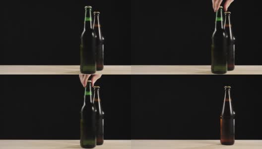 新鲜的啤酒。Hand从一张黑色背景的木桌上拿了一个绿色的瓶子，里面装着美味的精酿啤酒，旁边是棕色的瓶子，里面装着啤酒。冰镇新鲜啤酒与水滴。准备饮料。4 k高清在线视频素材下载