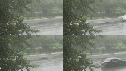 夏季大雨倾盆而下。在一棵绿色的大树和汽车的框架里。汽车在水坑中高速行驶，喷水。沥青上形成的巨大水坑高清在线视频素材下载