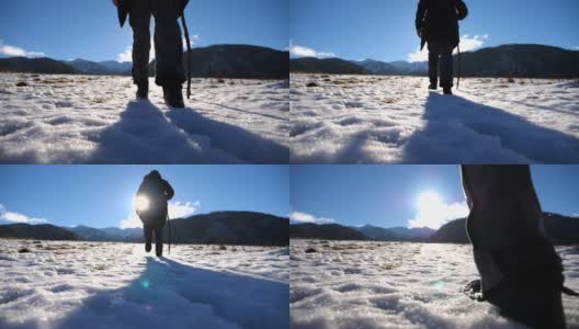 在阳光明媚的日子里，一个不认识的人用棍子爬上草地的雪山的后视图。年轻的徒步旅行者在雪地上徒步旅行，享受冬季旅行。健康积极的生活方式。慢动作高清在线视频素材下载
