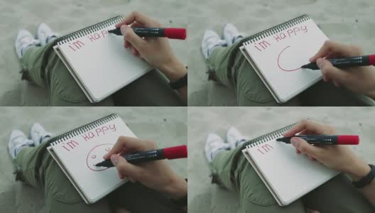 晚上，女孩在沙滩上用红色毡尖笔在笔记本上写着“我很快乐”，并画了一个笑脸高清在线视频素材下载