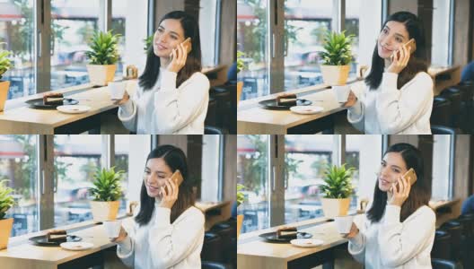 一个美丽快乐的女人，坐在靠窗的咖啡馆里，一边拿着一杯咖啡一边打电话高清在线视频素材下载
