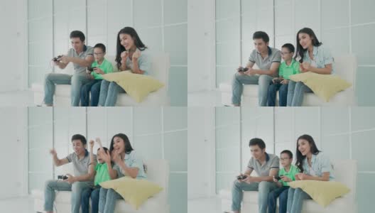 亚洲家庭的父亲和儿子一起在客厅玩电脑游戏与手机控制器，母亲是欢呼的玩家。高清在线视频素材下载