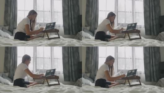 COVID-19大流行期间的在家教育。一名坐在卧室床上用笔记本电脑上在线课程的学生。少年学习。社会距离。高清在线视频素材下载