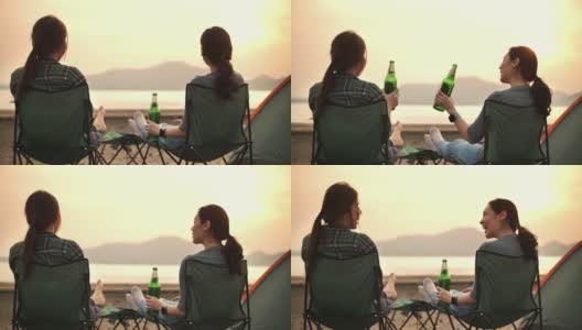 两个露营的女人喝着啤酒享受日落，看着美丽的山高清在线视频素材下载