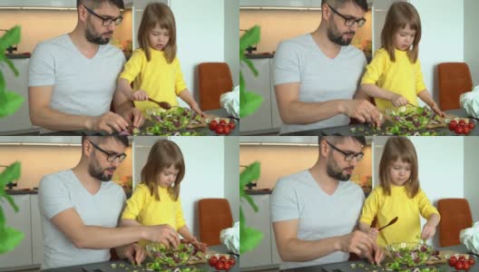 父亲和小女儿在厨房的餐桌上准备蔬菜、莴苣叶和西红柿沙拉。小女孩帮忙做饭。高清在线视频素材下载