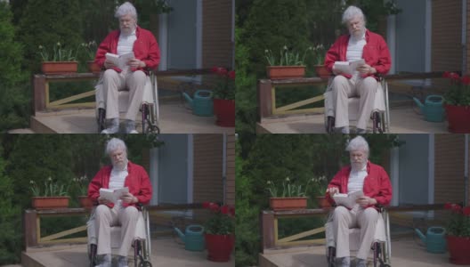 老年残障智人在阳光明媚的户外，坐在轮椅上看书。享受嗜好的白种人受损退休人员的广角正面照片。生活方式和残疾。高清在线视频素材下载