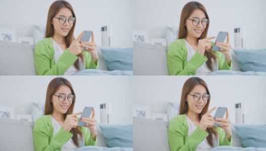 亚洲美女戴着眼镜，在家里用手机聊天。漂亮的年轻女孩坐在沙发上，在客厅用智能手机上网查看好消息后感到兴奋和快乐。高清在线视频素材下载