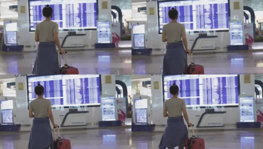 一名年轻女子在国际机场走向航班信息牌，手里拿着护照和行李箱，查看她的航班时间高清在线视频素材下载