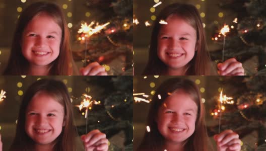 可爱的小女孩附近的圣诞树树枝与孟加拉灯的背景闪闪发光的花环。快乐小孩许下新年愿望，等待圣诞老人和奇迹。快乐的童年高清在线视频素材下载