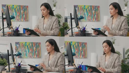 在一家大公司里，一位尽职尽责的办公室职员坐在办公桌前，用平板电脑和电脑同步文档，比较数据，点击屏幕，滚动屏幕，专注于她的工作高清在线视频素材下载