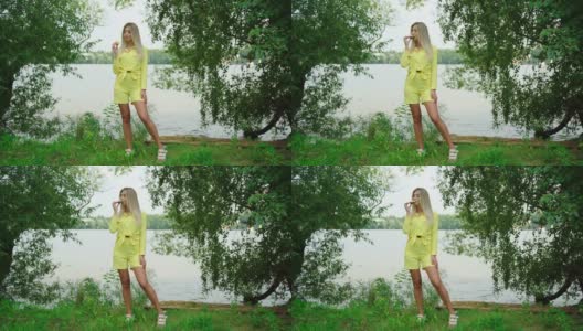 美丽的金发微笑女人享受暑假在池塘。模特穿着黄色的衣服，拿着一片黄色的西瓜。漂亮女孩吃新鲜食物的肖像。高清在线视频素材下载