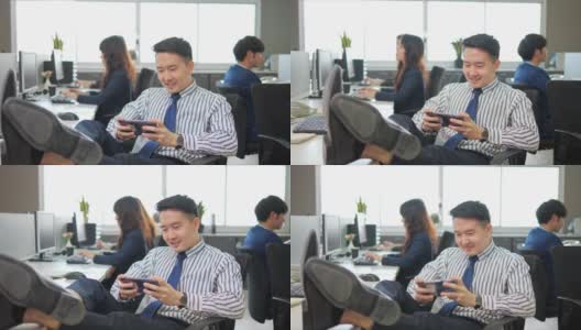 懒惰的亚洲商人玩着游戏打发工作时间在办公室打电话，同事履行职责高清在线视频素材下载