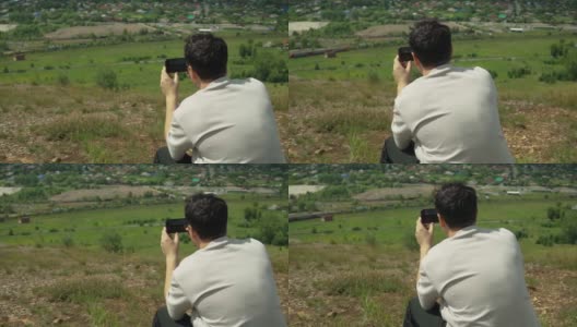 一名年轻的成年男子在一座大山的山顶用智能手机拍照高清在线视频素材下载