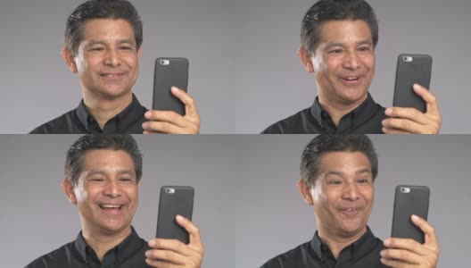 高级男子用手机视频通话，笑着，孤立在灰色背景中。穿着黑衬衫的亚洲人。高清在线视频素材下载