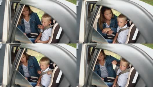 特写的母亲系她的小儿子在汽车座椅上的安全带在汽车里。高清在线视频素材下载