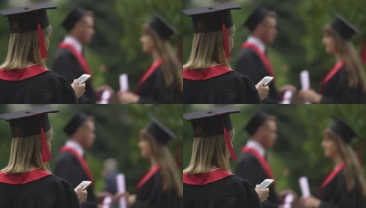 金发女孩穿着学位服，戴着毕业帽在智能手机上上网高清在线视频素材下载