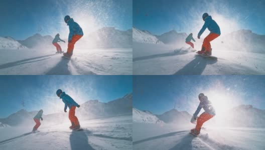 SLO MO TS两名滑雪板运动员在阳光下沿着雪道滑行，使雪颗粒在空中飞舞高清在线视频素材下载