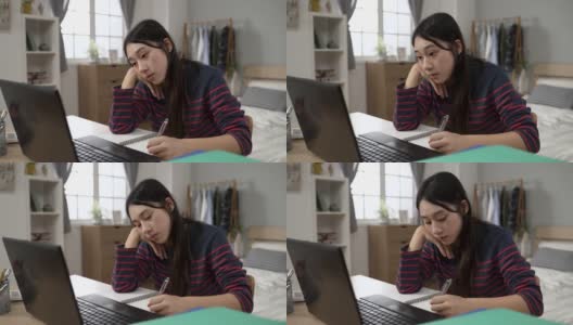 昏昏欲睡的亚洲年轻成年学生拿着笔，托着脸，在家里在卧室里用电脑上在线课程。高清在线视频素材下载