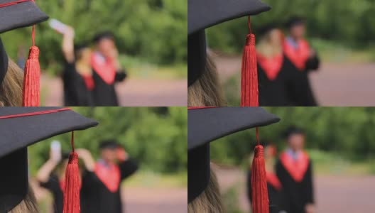 女士戴着学术帽看着快乐的朋友毕业生在公园里玩高清在线视频素材下载