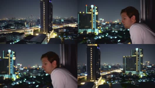一名忧伤、焦虑的年轻人在夜晚望着窗外的城市灯光高清在线视频素材下载