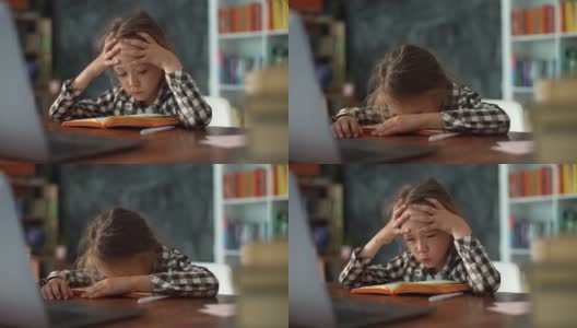 特写镜头中，精疲力竭、心烦意乱的小学生女孩在家里用头撞桌子，写着困难的作业。高清在线视频素材下载
