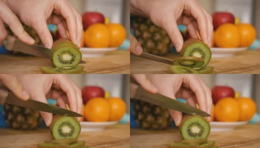 男子用刀在木板上切猕猴桃，背景是水果和蔬菜。特写镜头。高清在线视频素材下载
