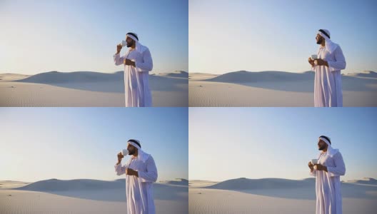 早上好，在蓝天和沙丘的映衬下，在巨大的沙漠中喝咖啡的男性酋长高清在线视频素材下载