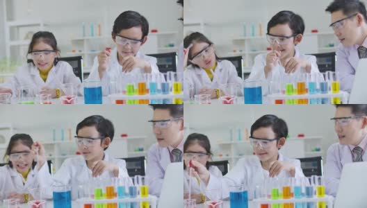 小学科学课堂:亚洲儿童在科学实验室实验台上统一学习各种颜色的试管玻璃水。高清在线视频素材下载