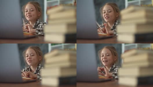 在笔记本电脑上通过视频电话会议在线学习时，微笑的小学女孩与在线老师交谈的特写。高清在线视频素材下载
