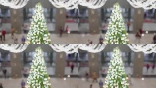 一棵挂着许多灯泡的圣诞树挂在室内。这些是用来做圣诞装饰的。模糊的背景是人们进入或离开建筑。的焦点。在看。在屏幕的中心是一棵绿色的圣诞树。高清在线视频素材下载