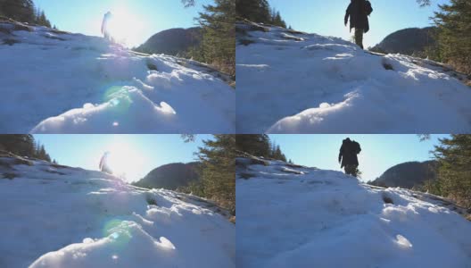 在冬季的旅途中，一个不知名的游客在雪坡上攀爬。在阳光明媚的日子里，年轻的徒步旅行者在山林中行走。背景是阳光。旅行的概念。后视图慢动作高清在线视频素材下载