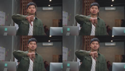 不高兴的亚洲商人看着相机和做拇指向下的手势在创意办公室。高清在线视频素材下载