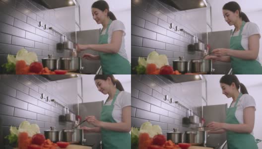 快乐开朗的亚洲妻子穿着围裙在厨房为家人做饭，亚洲女性练习烹饪食谱在家隔离周末活动高清在线视频素材下载