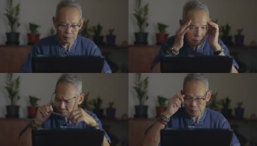 疲惫的亚洲老人坐在办公桌前，摘下眼镜，放下笔记本电脑，按摩太阳穴，缓解长期使用现代设备后的疲劳。由于电脑工作过度而头痛。高清在线视频素材下载